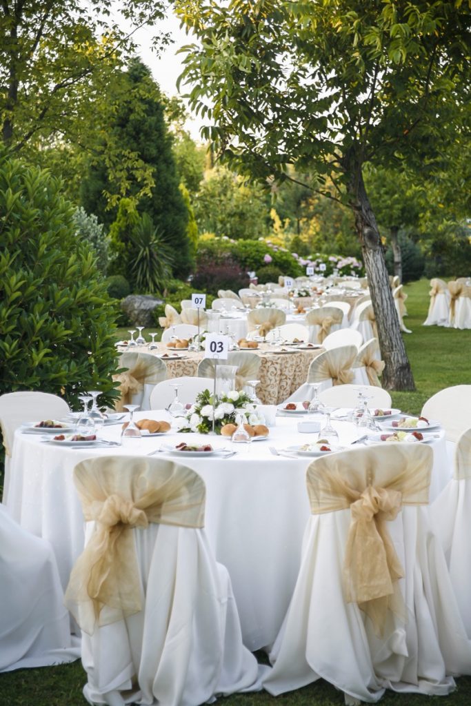 Absolutely-Delicious reception outdoors can be elegant. These row of tables and chairs dressed in white and gold look beautiful.
