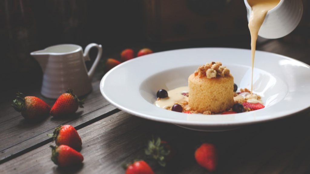 Absolutely Delicious presents a pouring of creamy sauce onto a bowl containing a shortcake.