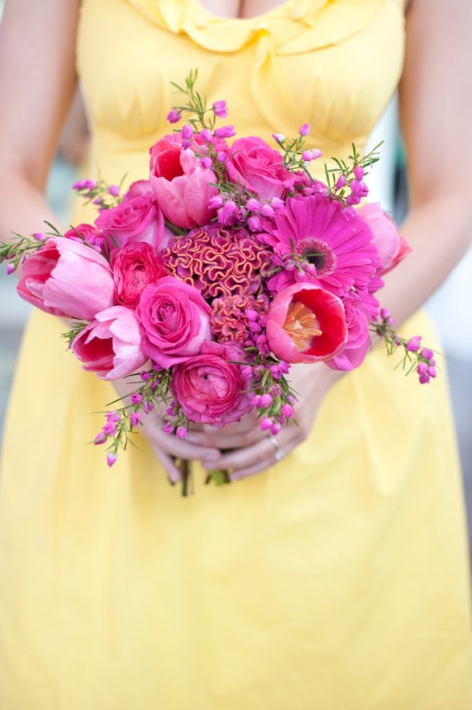 Alamo Plants & Petals presents a woman in yellow holding a bouquet of magenta-hued flowers