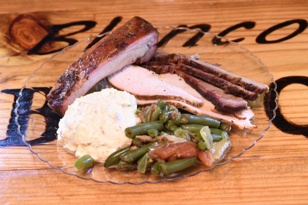 Blanco BBQ on a bridal plate containing a serving of Brisket, a Rib, Turkey, potato salad, and some green beans.