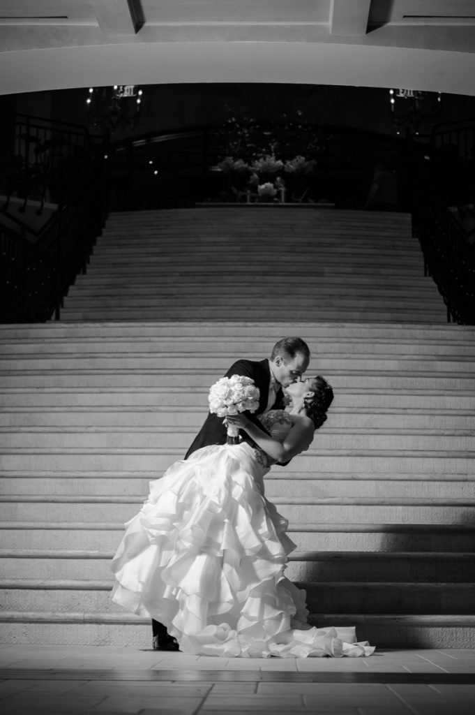 a dramatic black and white photo of a man kissing a woman in front of the staircase in the lobby at The Eilan Hotel Resort and Spa.
