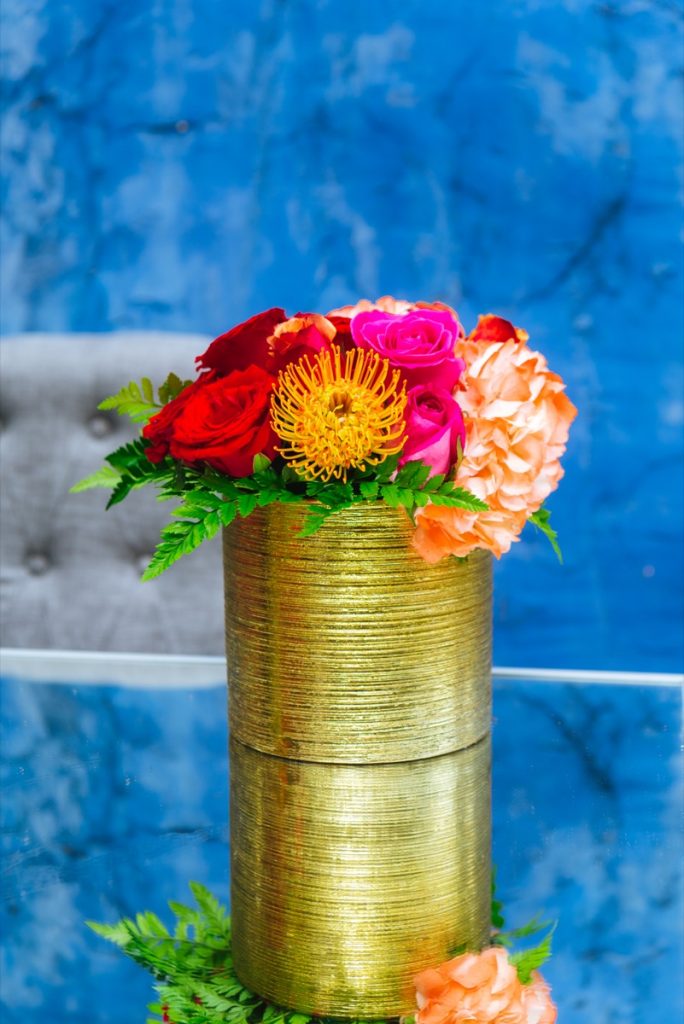 A Freesia Designs centerpiece that is a gold-wire pot toped with red orange and yellow flowers!