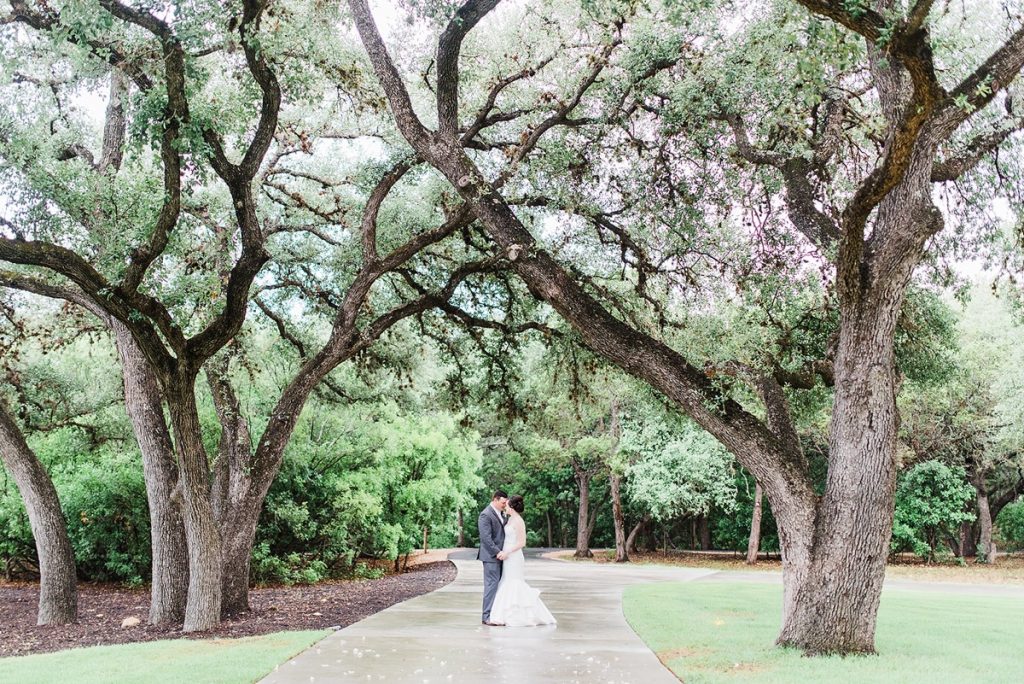 A woman and a man are canoodling along a path outside, surrounded by trees at The Chandelier of Gruene.