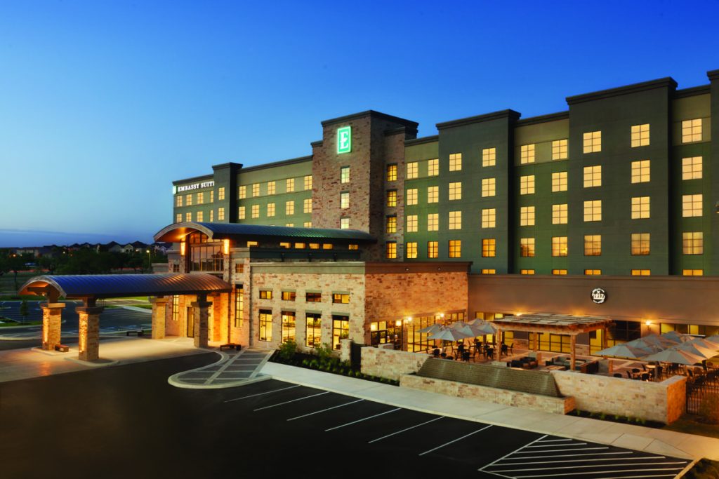 The outside of Embassy Suites by Hilton Brooks Hotel, slight dusk, lights are on.