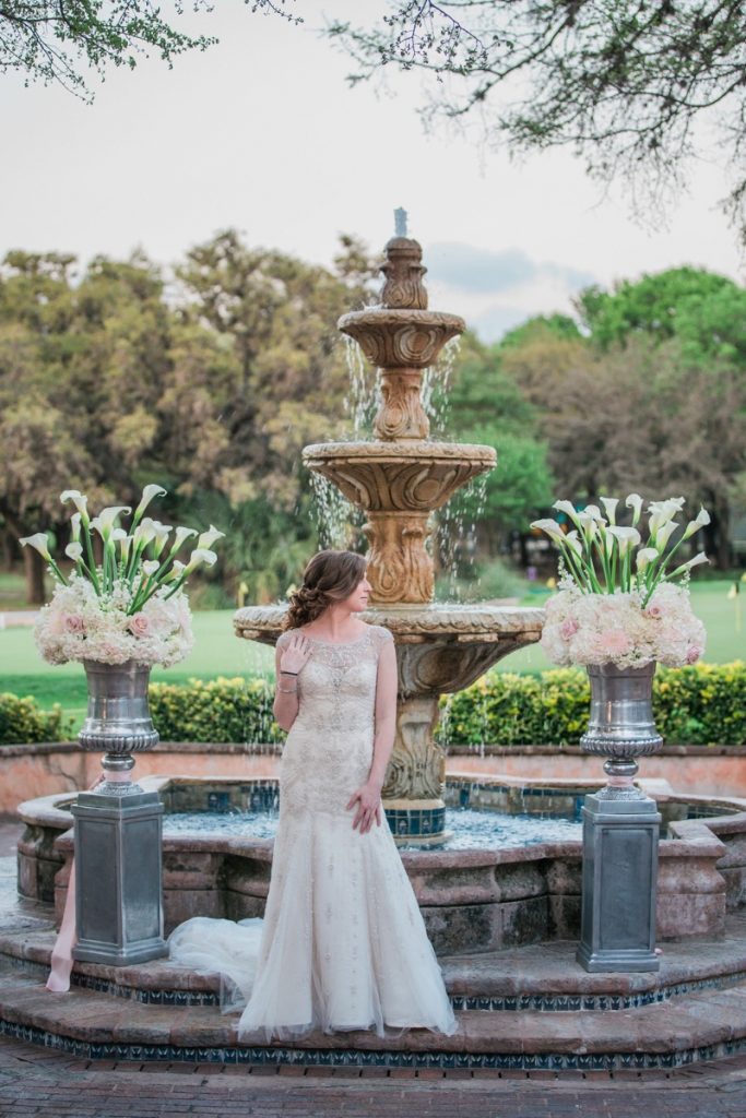 A bride poses at the fountain in the back patio of The Dominion.