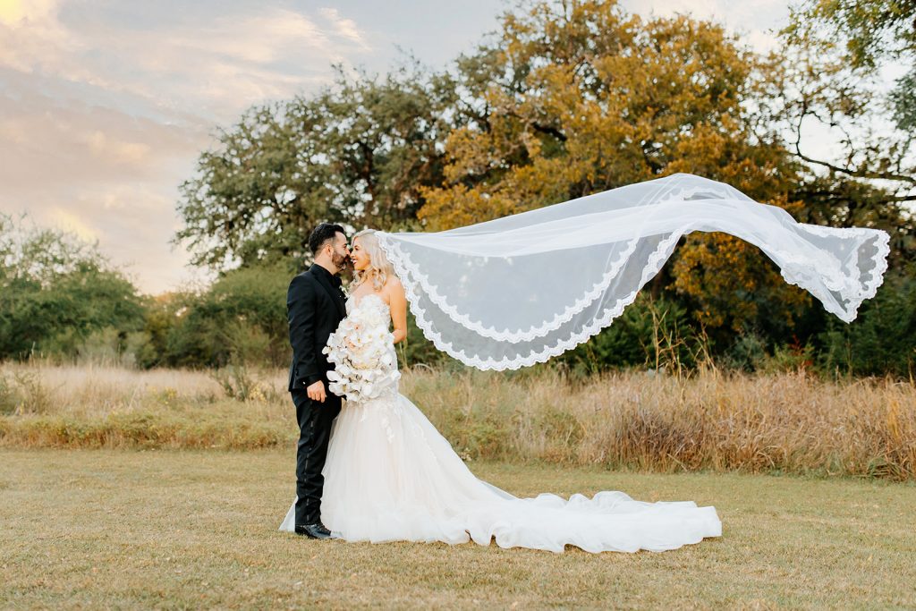groom and bride with veil flying in the wind with Texas sunset behind them